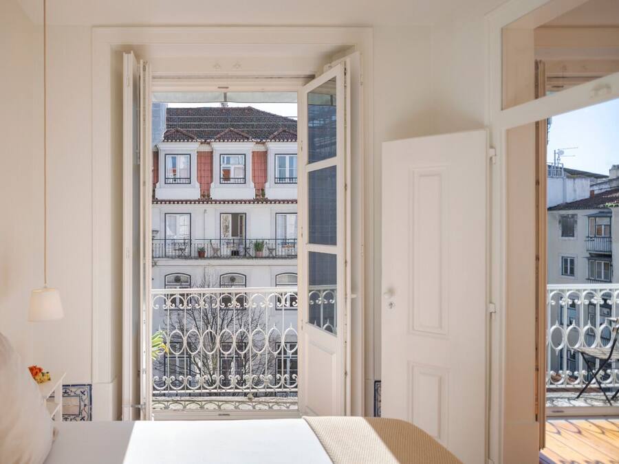 Un dormitorio con cama, mesita de noche, lámpara y vistas a un balcón con barandilla.