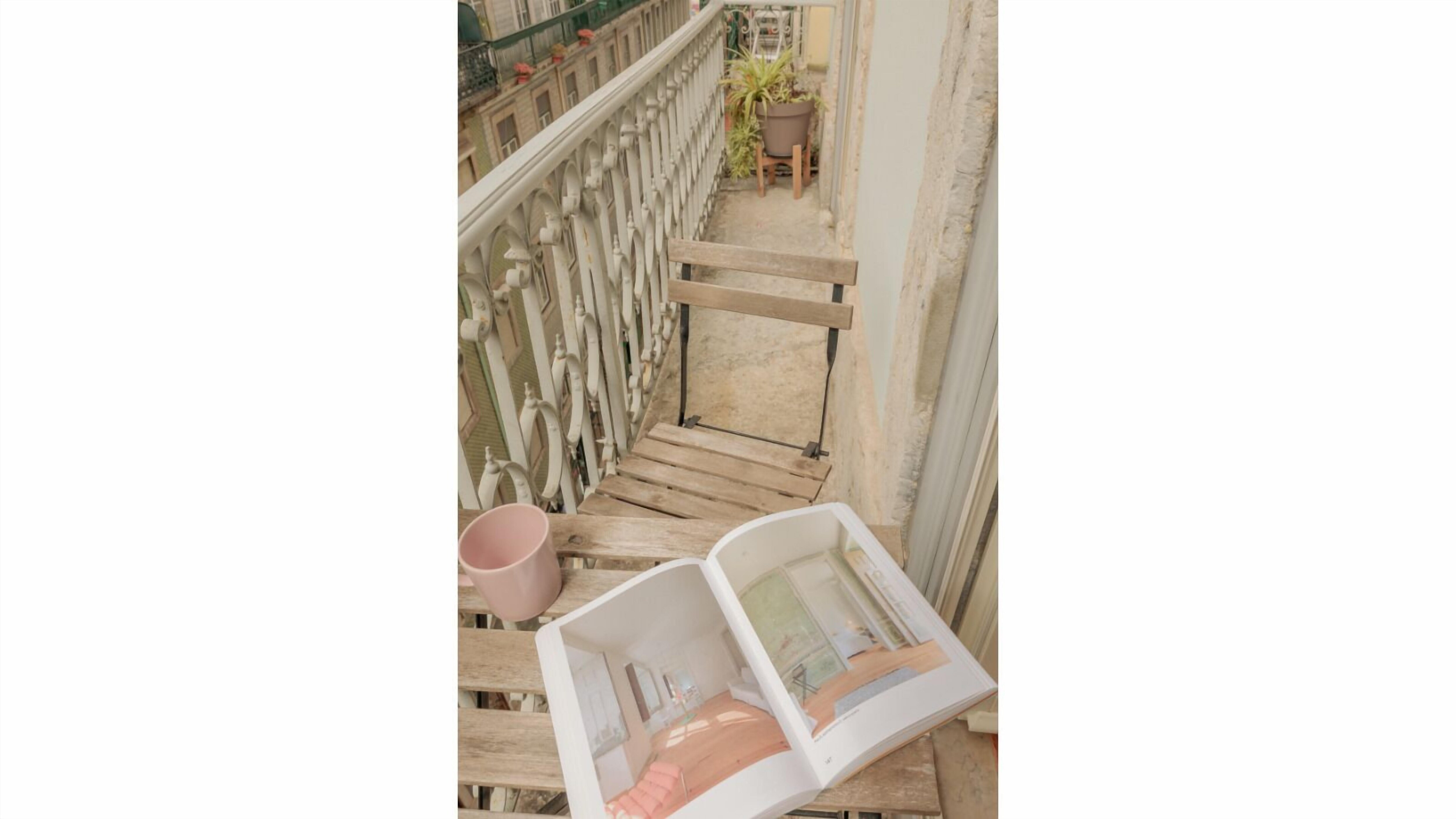 A wooden bench with a magazine, a pink mug, and a potted plant on a balcony.