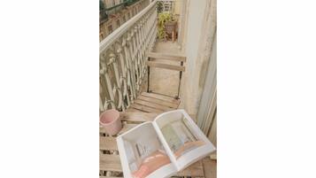 A wooden bench with a magazine, a pink mug, and a potted plant on a balcony.