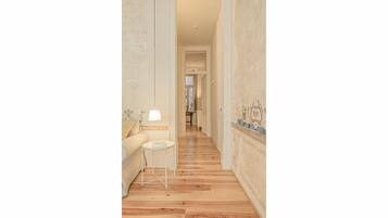 Un couloir avec un plancher en bois, un canapé blanc, une petite table et une lampe.