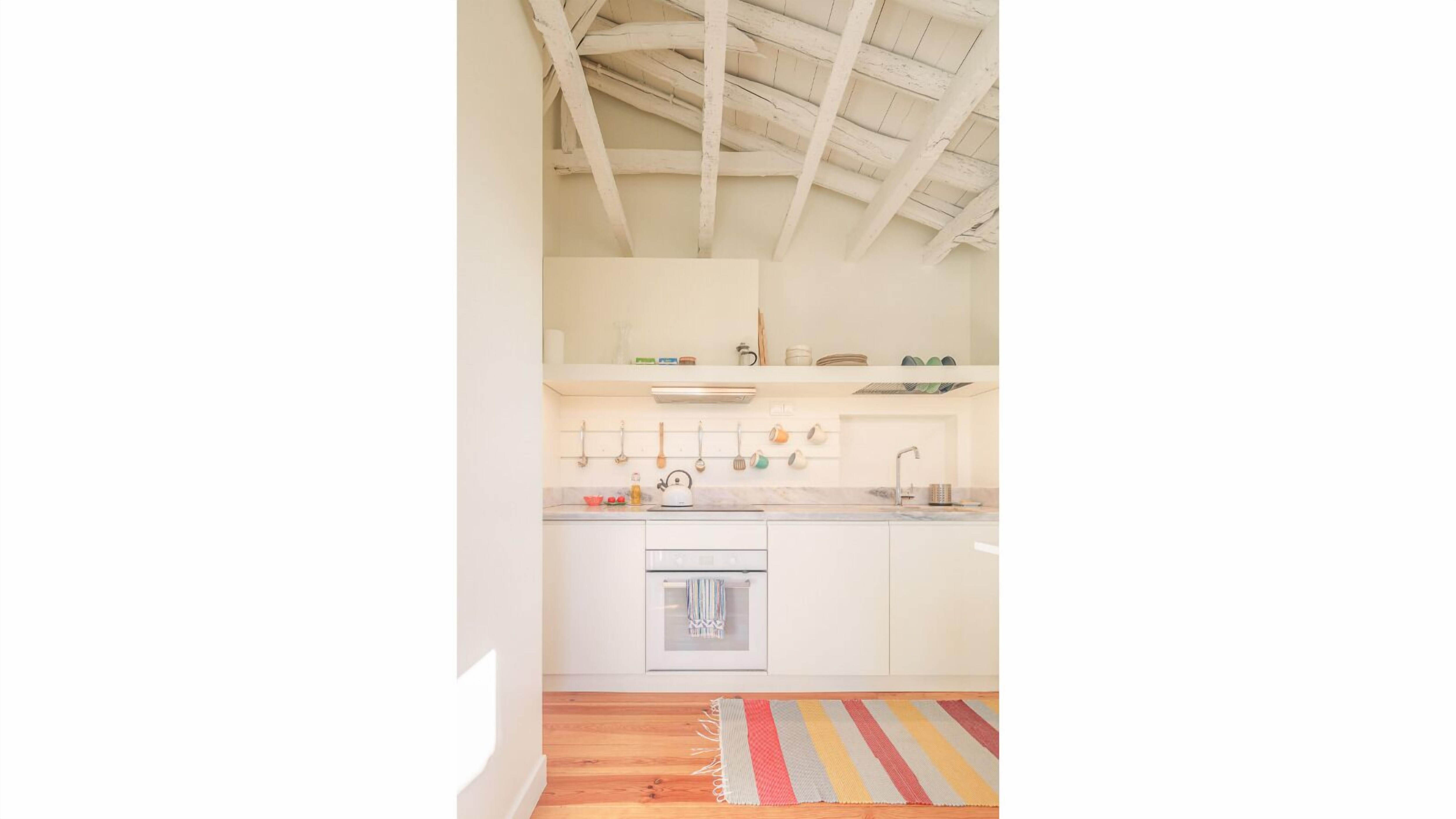 Una cocina con armarios blancos, piso de madera y una alfombra colorida.