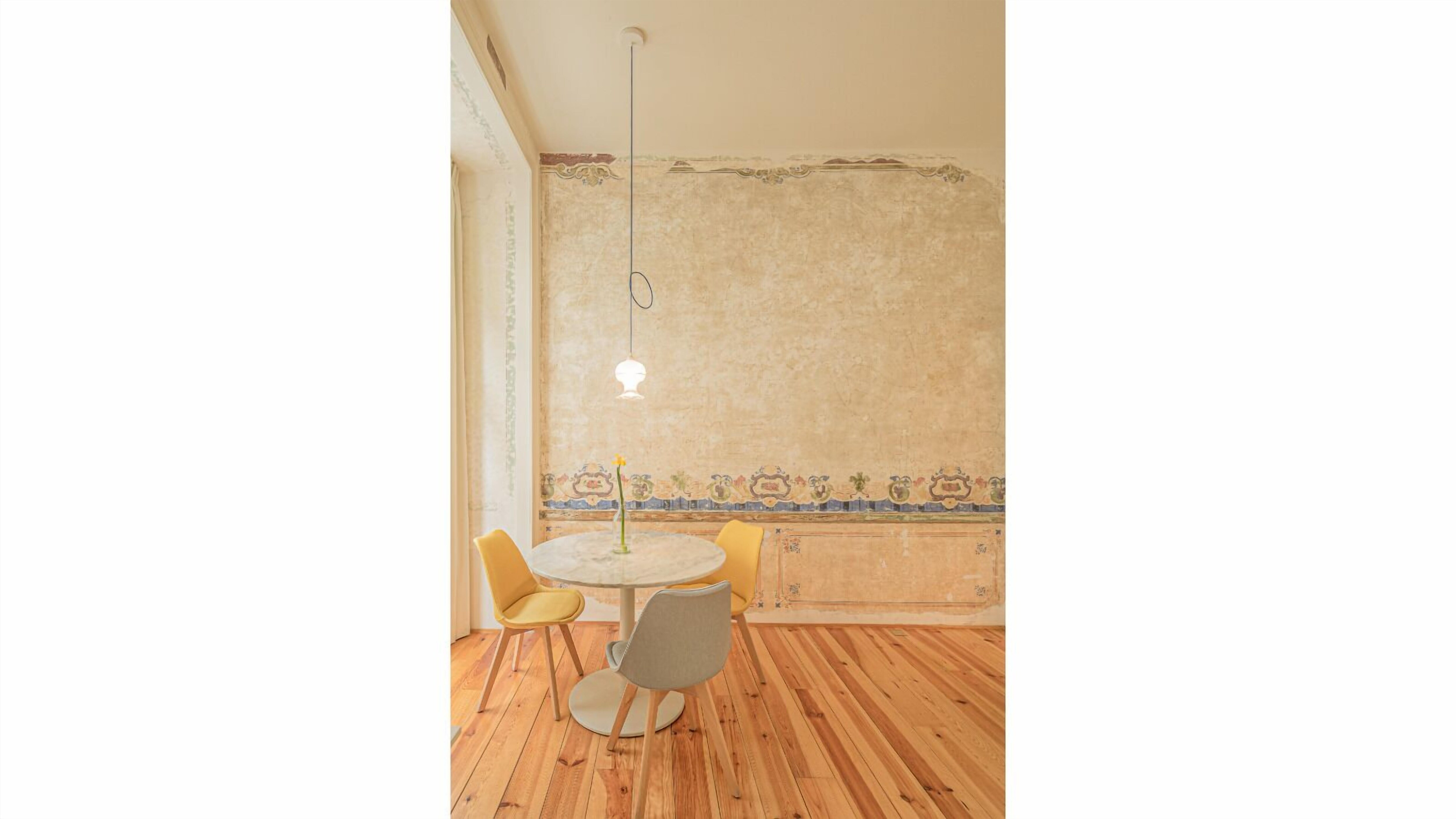Een kamer met een ronde tafel, twee stoelen, een hanglamp en een patroon op de muur.