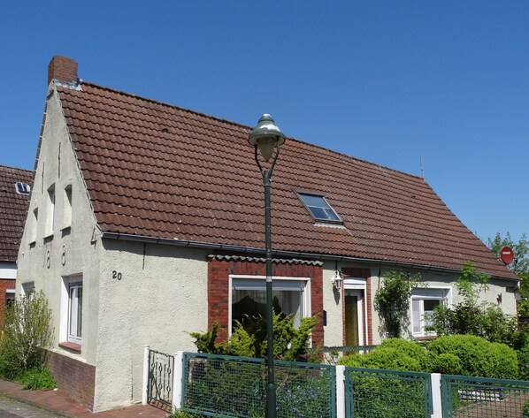 Une maison avec un toit recouvert de tuiles rouges, une petite fenêtre et une clôture verte.
