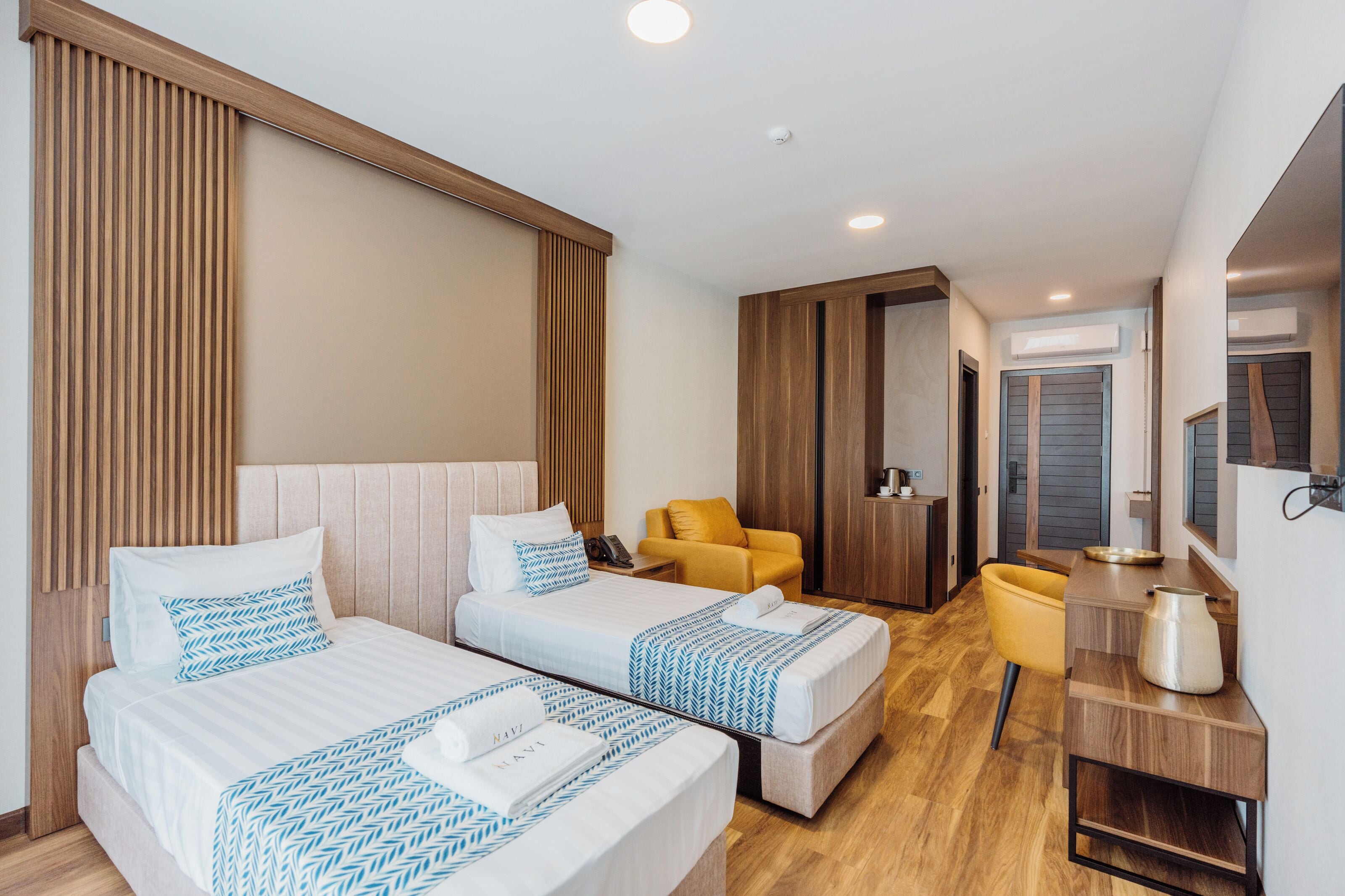 Een hotelkamer met twee bedden, een gele stoel, een klein tafeltje en een spiegel.