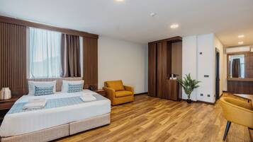 Una habitación de hotel moderna con una cama grande, un sillón amarillo, una mesita y una planta en maceta.
