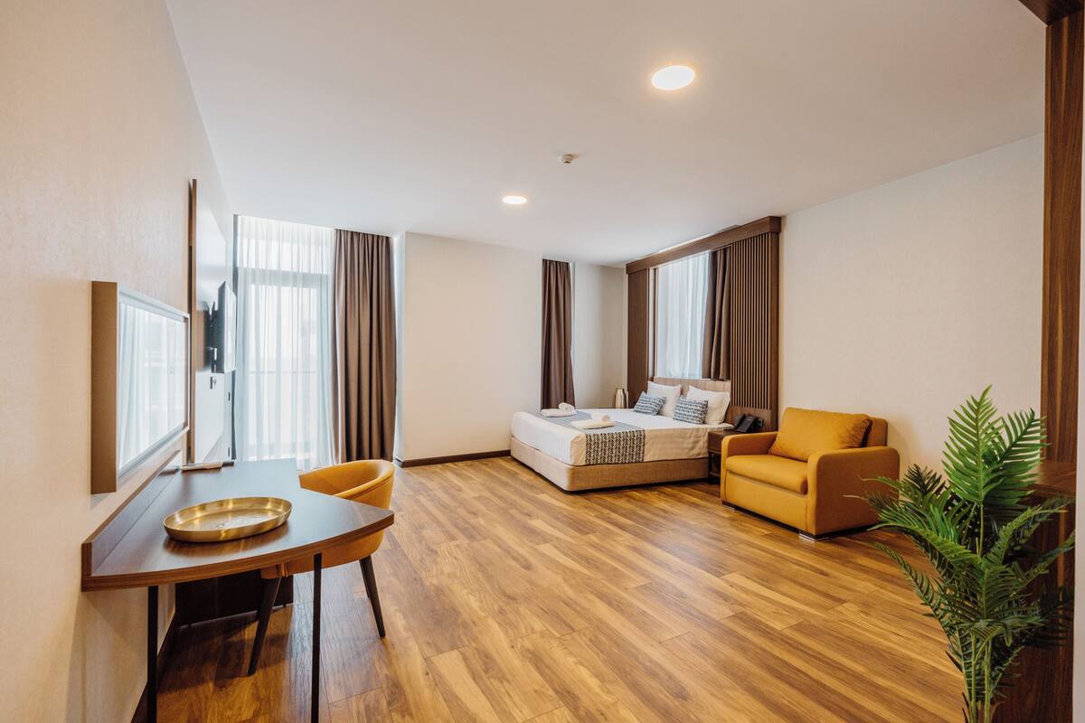 Quarto de hotel com cama, sofá, mesa de jantar e planta em vaso.