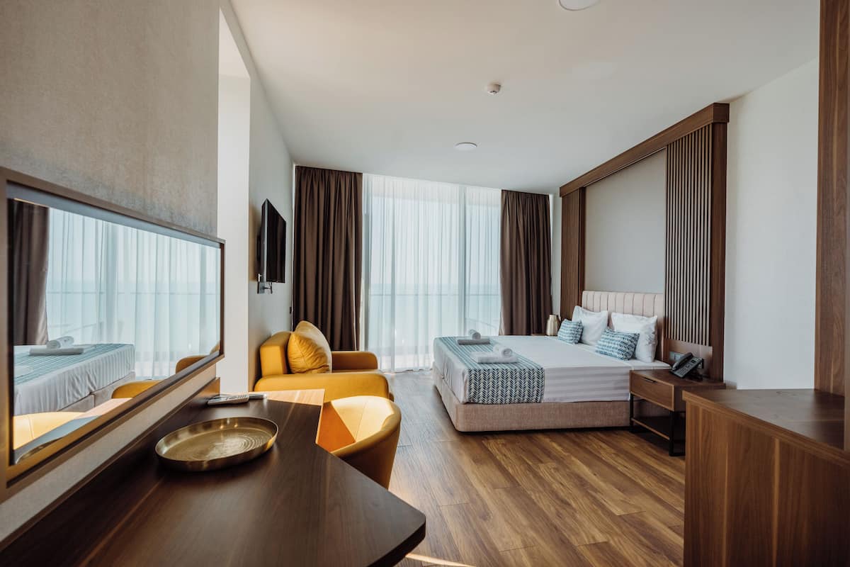 Quarto de hotel com cama, sofá, escrivaninha e um espelho grande.