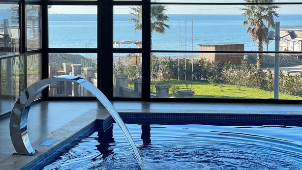 A pool with a water feature, large windows, and a view of the sea. - Hotel Navi (Batumi)