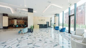 A modern hotel reception area with a marble floor, comfortable seating, and a large window offering a view of the outside. - Hotel Navi (Batumi)