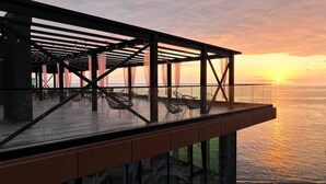 An outdoor terrace with a view of the sunset over the ocean, featuring a wooden deck and metal chairs. - Hotel Navi (Batumi)