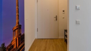 Un pasillo con una puerta blanca, suelo de madera y un interruptor de luz en la pared.