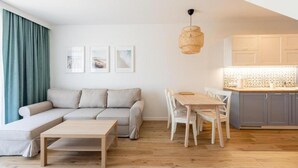 A modern living room with a sofa, a dining table, and chairs, a kitchen with cabinets, and a hanging light fixture. - Comfortable, 2-level holiday apartment (Grzybowo)