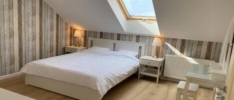 Ein Schlafzimmer mit Oberlichter, Holzwänden, einem Bett, Nachttischen, einem Spiegel und einem Heizkörper.