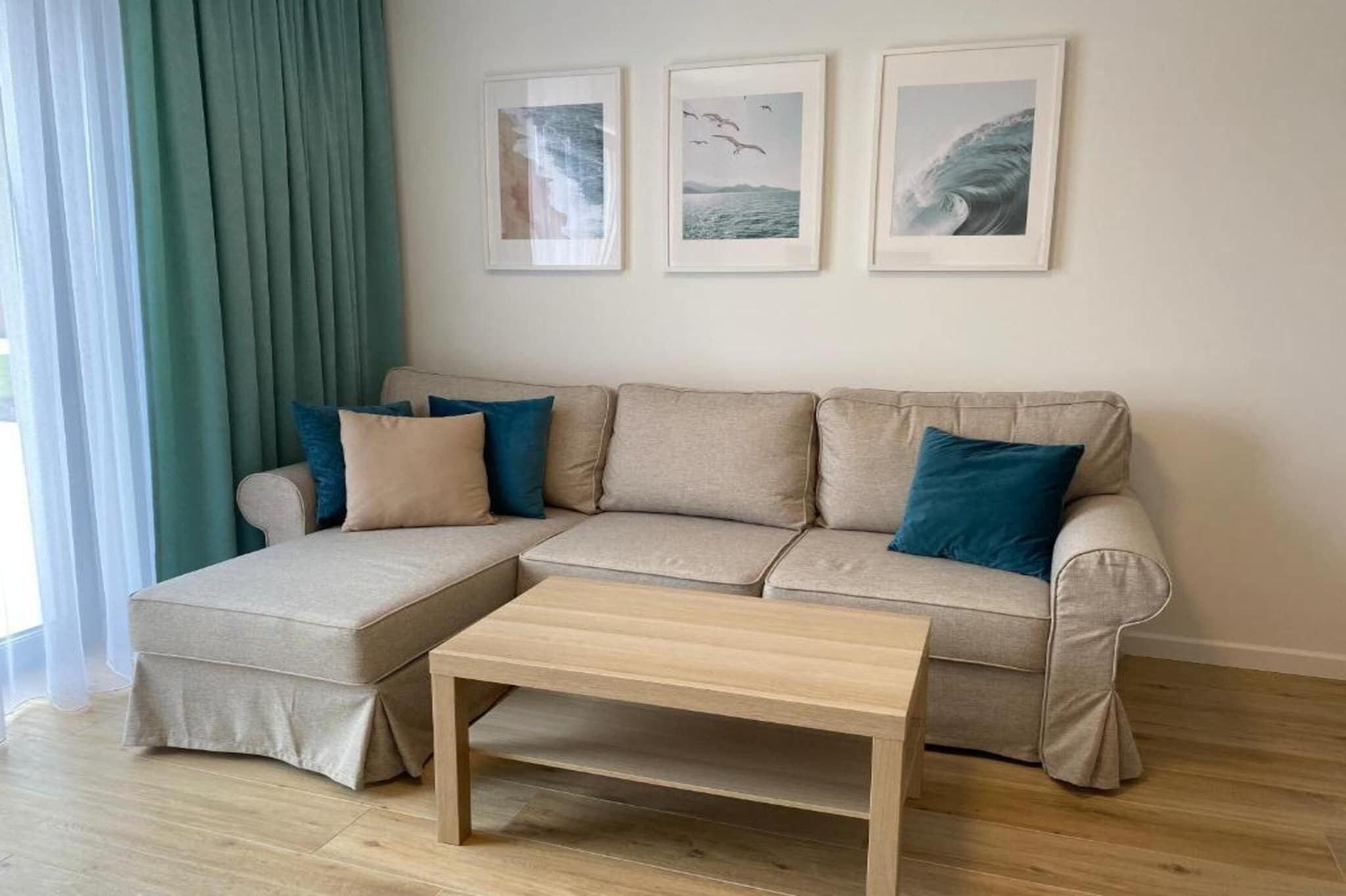 A living room with a beige sectional sofa, a wooden coffee table, and three framed pictures on the wall.