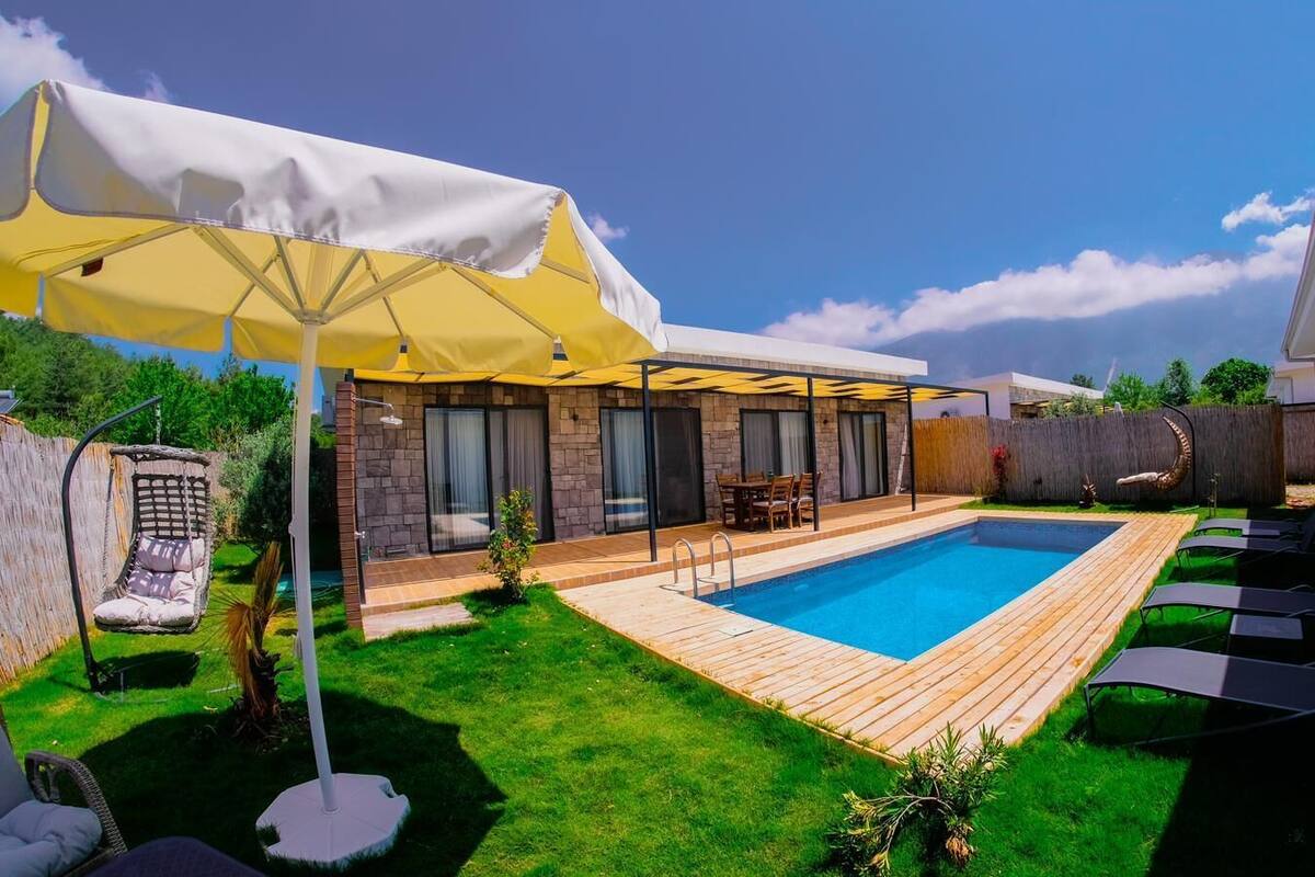 A backyard with a swimming pool, a wooden deck, a hanging chair, and a covered patio area.