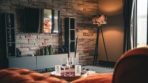 Un salon moderne avec un mur en briques, un téléviseur à écran plat, un lampadaire et un confortable canapé orange.