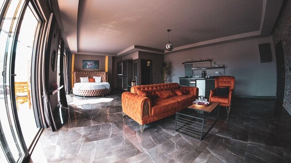Amplia sala de estar con una cama grande, un sofá y una mesa de centro. Hay una zona de cocina con un fregadero y un refrigerador.