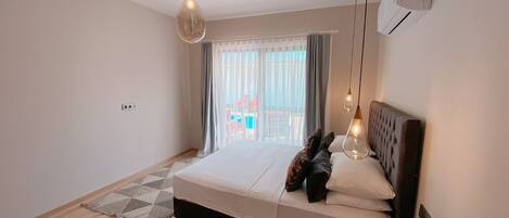 Une chambre à coucher avec un lit, deux lampes suspendues, une fenêtre avec des rideaux et une vue sur l’extérieur.