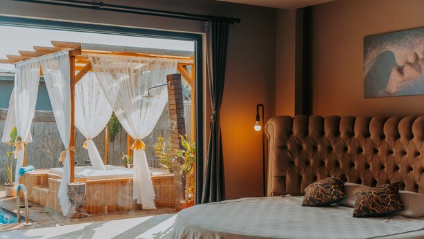 Une chambre avec un grand lit, une vue sur une terrasse en bois et un luminaire fixé au mur.