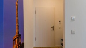 Un couloir avec une porte blanche, un thermostat et une petite table.