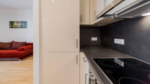 Une cuisine moderne avec une plaque de cuisson noire, des armoires blanches et un canapé rouge dans le salon attenant.