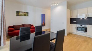 Un salon moderne avec un canapé rouge, une table en verre et des chaises noires. On y trouve également un coin cuisine avec des meubles blancs et une cuisinière.