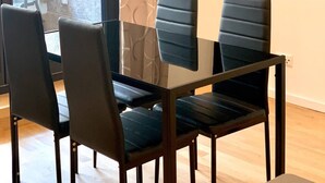 A modern living room with a glass dining table, four black chairs, a flat-screen TV mounted on the wall, and a large window with a view of the outside. - ENJOY new flat in MITTE for couples and families
 (Berlin)
