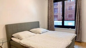 A single bed with a grey headboard, a grey patterned duvet, and a window with curtains. - ENJOY new flat in MITTE for couples and families
 (Berlin)