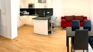 A modern kitchen with white cabinets, a black countertop, and a stainless steel range hood. There is a red sofa and blue chairs in the living area. - ENJOY new flat in MITTE for couples and families
 (Berlin)