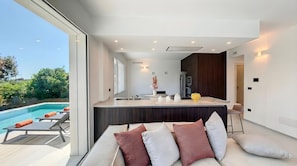 A modern kitchen with a central island, a dining area with a sofa and cushions, and a view of a swimming pool. - 5-star dream villa, beach access, pool, jacuzzi (Marina di Felloniche)