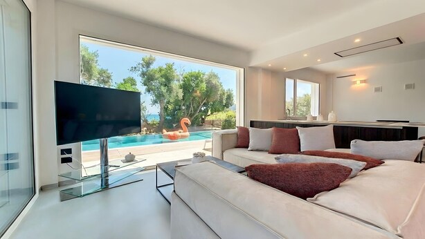 A modern living room with a large TV, a sofa, and a view of a swimming pool. - 5-star dream villa, beach access, pool, jacuzzi (Marina di Felloniche)