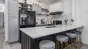Una cocina moderna con una isla grande, armarios grises, un refrigerador negro y un grifo dorado.