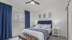 Un dormitorio con una cama grande, una mesita de noche, un banco y un ventilador de techo.