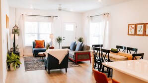 A modern living room with a sofa, a coffee table, and a dining area with chairs and a table. - Artist Retreat | Near Downtown, Stadium & UGA (Athens)