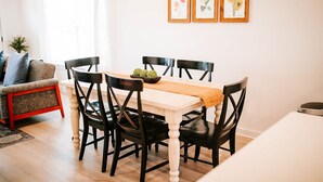 A dining area with a wooden table, black chairs, and a white table runner. There are three framed botanical prints on the wall above the table. - Artist Retreat | Near Downtown, Stadium & UGA (Athens)
