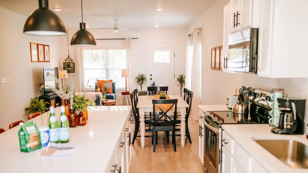A modern kitchen with a central island, wooden cabinets, and a dining area with a table and chairs. - Artist Retreat | Near Downtown, Stadium & UGA (Athens)