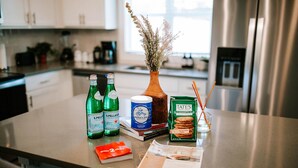 Eine Küchenarbeitsplatte mit verschiedenen Gegenständen, darunter zwei Flaschen S. Pellegrino Wasser, eine Dose Mama's Boy Kaffee, eine Packung Kekse von Tate's Bake Shop, ein Buch und eine Vase mit getrockneten Blumen.