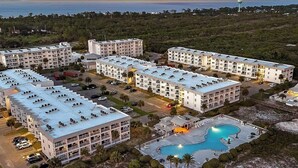 Un resort con varias edificaciones, una piscina y vista al océano al atardecer.