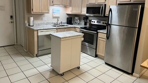 Una cocina compacta con armarios de madera clara, un refrigerador de acero inoxidable, un microondas, un horno y una pequeña isla con un lavamanos.