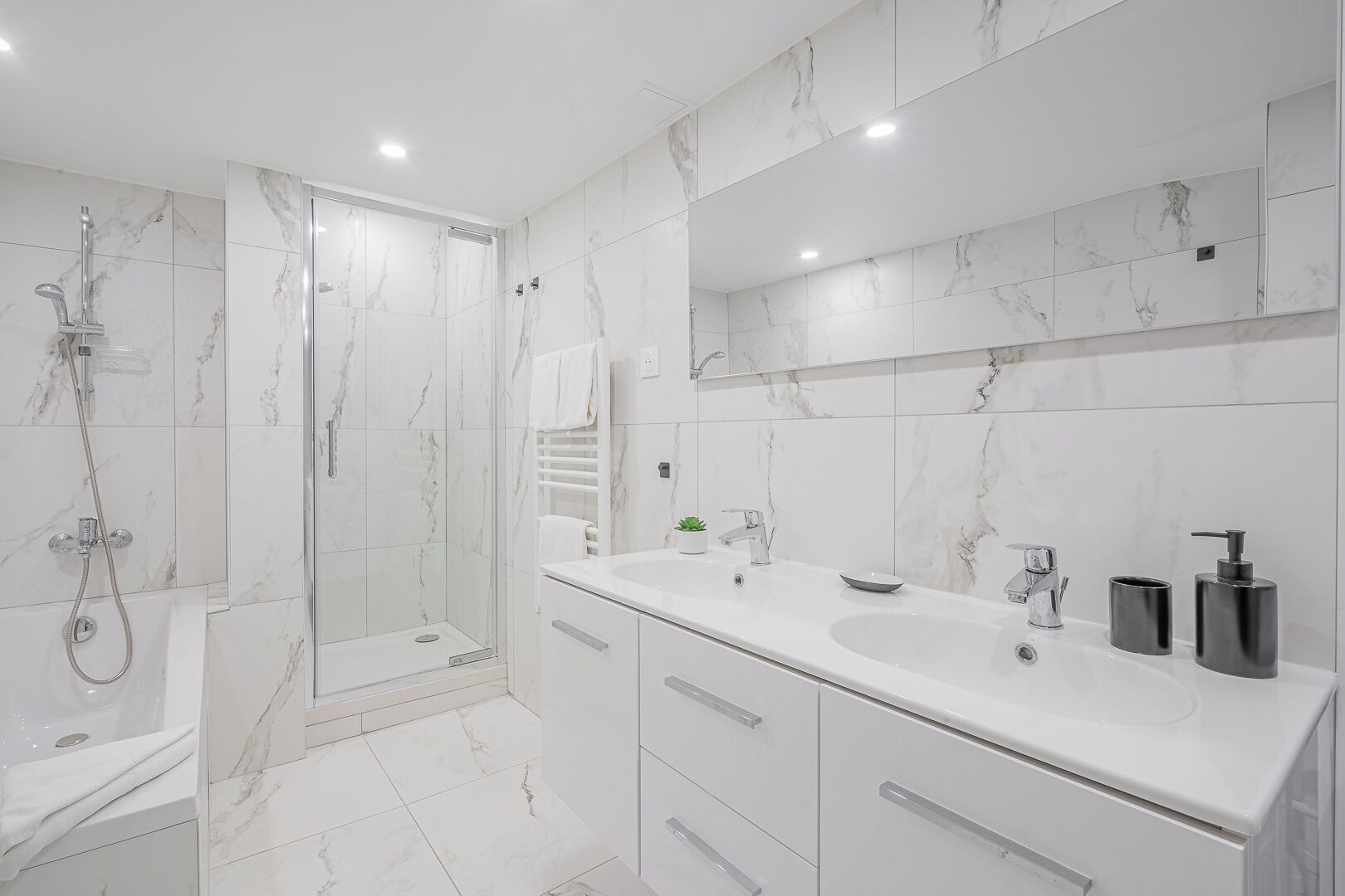 A modern bathroom with a walk-in shower, a bathtub, a large mirror, and a vanity with a sink and toiletries.
