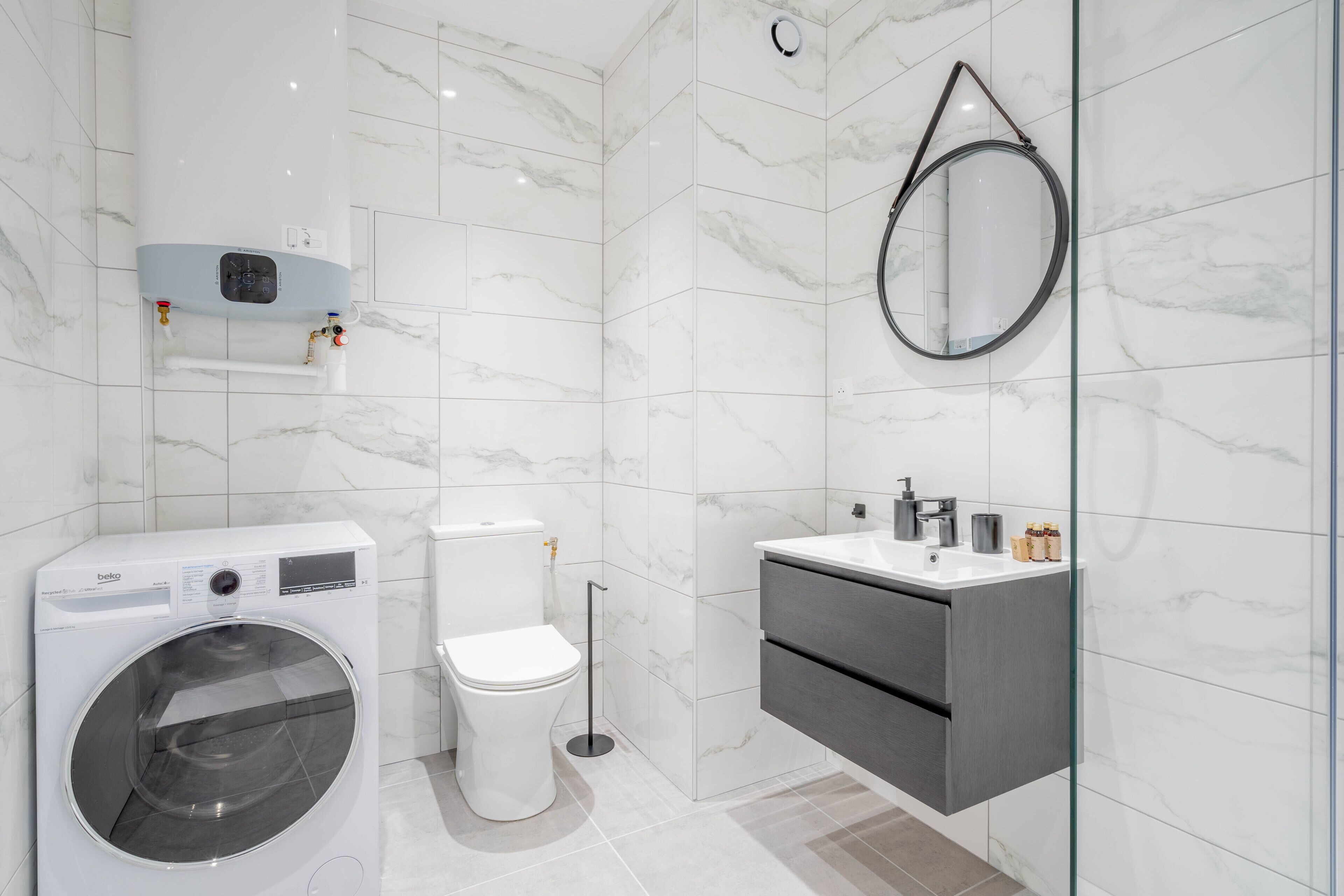 A modern bathroom with a washing machine, toilet, and a vanity with a mirror.