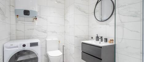 A modern bathroom with a washing machine, toilet, and a vanity with a mirror.