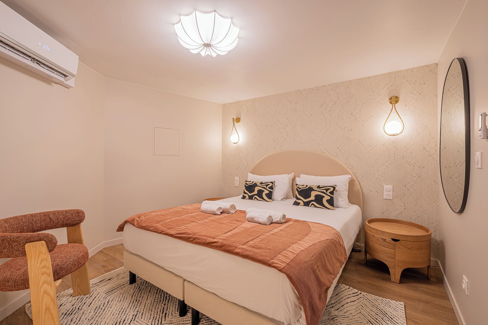 Une chambre à coucher comprenant un lit, une chaise, une table de chevet et un miroir fixé au mur.