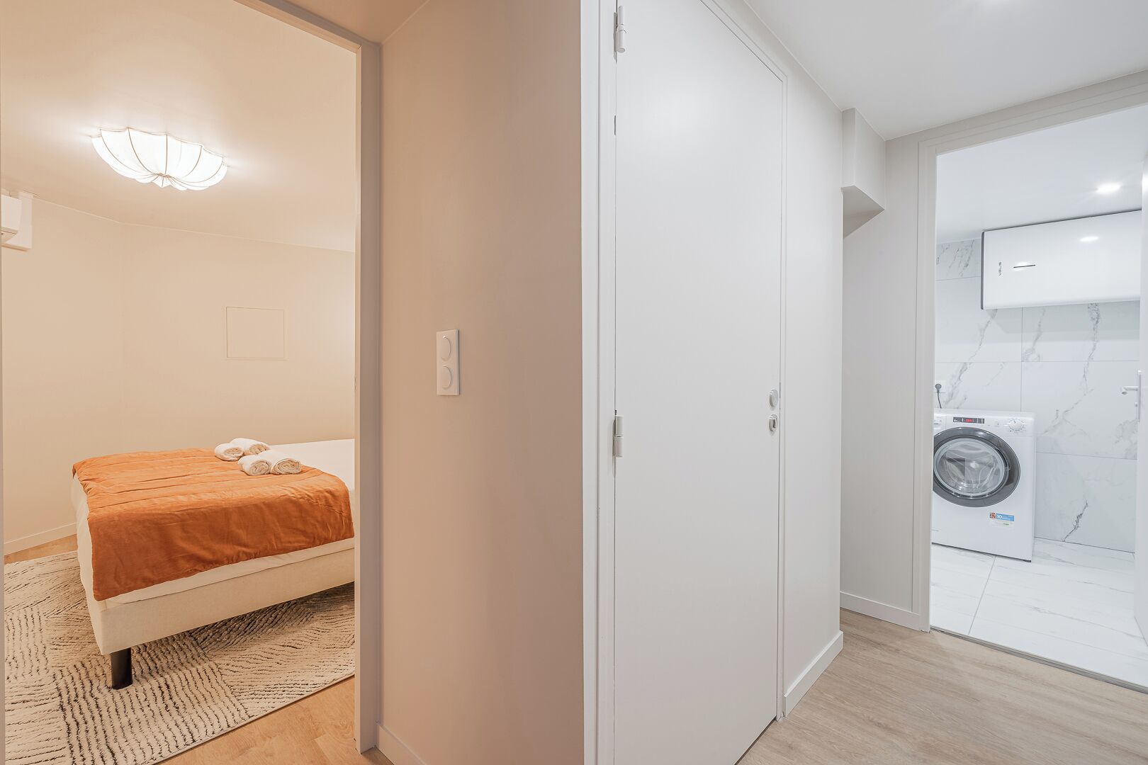 A bedroom with a bed, a washing machine, and a bathroom with a mirror and toilet.