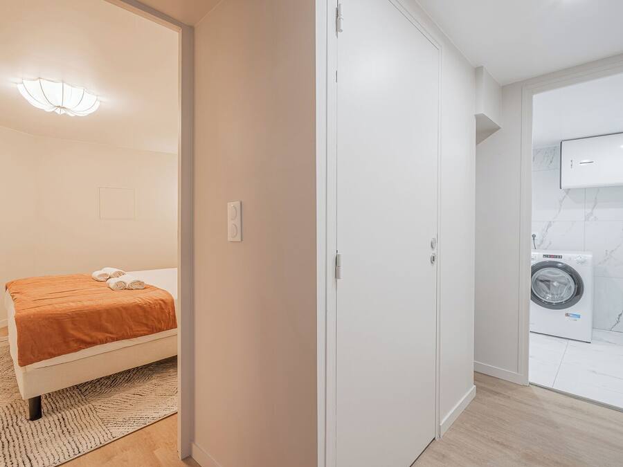 A bedroom with a bed, a washing machine, and a bathroom with a mirror and toilet.