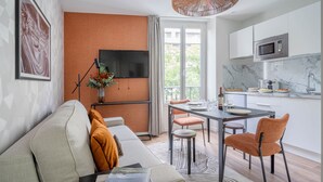 Un saló modern amb un sofà, una taula de dinar amb cadires, un televisor fixat a la paret i una zona de cuina amb microones.