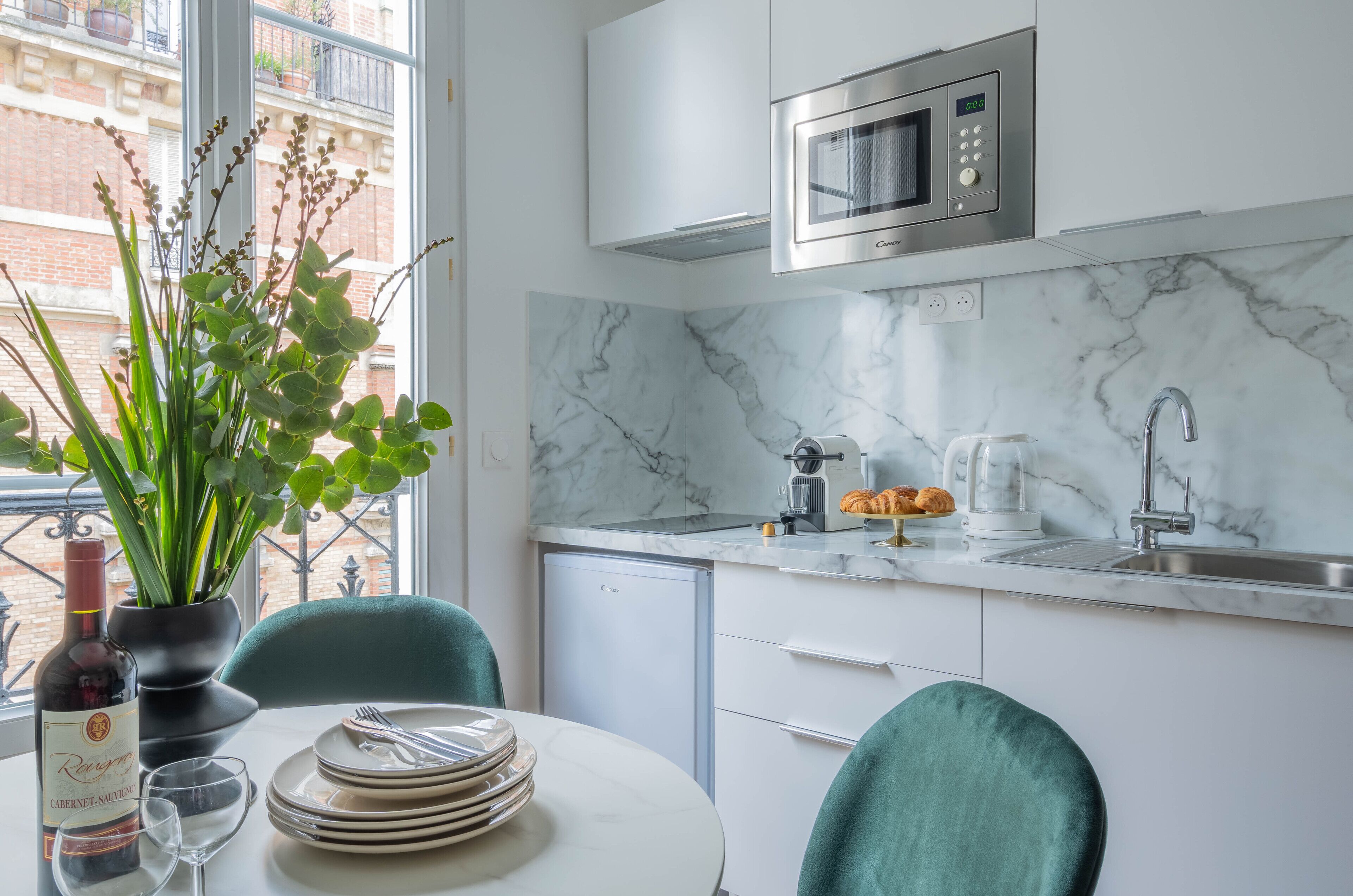 A modern kitchen with a built-in microwave, a coffee maker, and a sink. There is a dining table with plates and a bottle of wine.