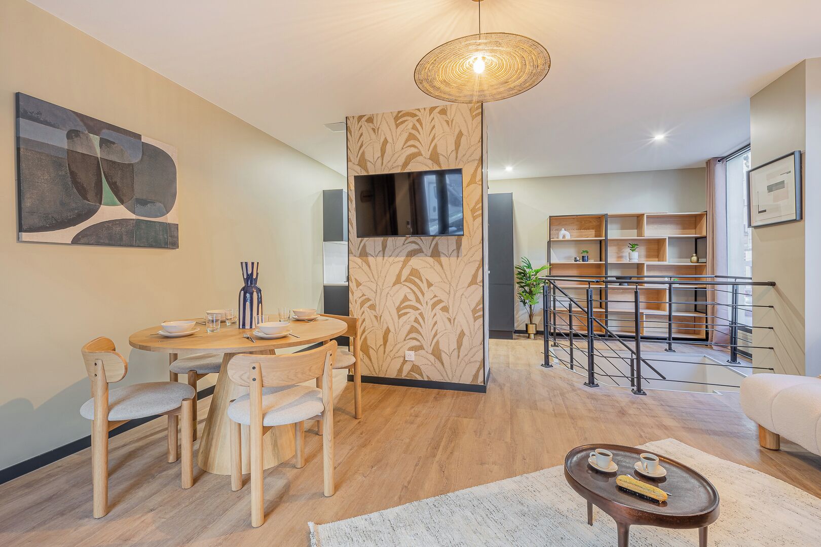 A modern living room with a dining area, a TV mounted on a wall, and a staircase leading to another level.