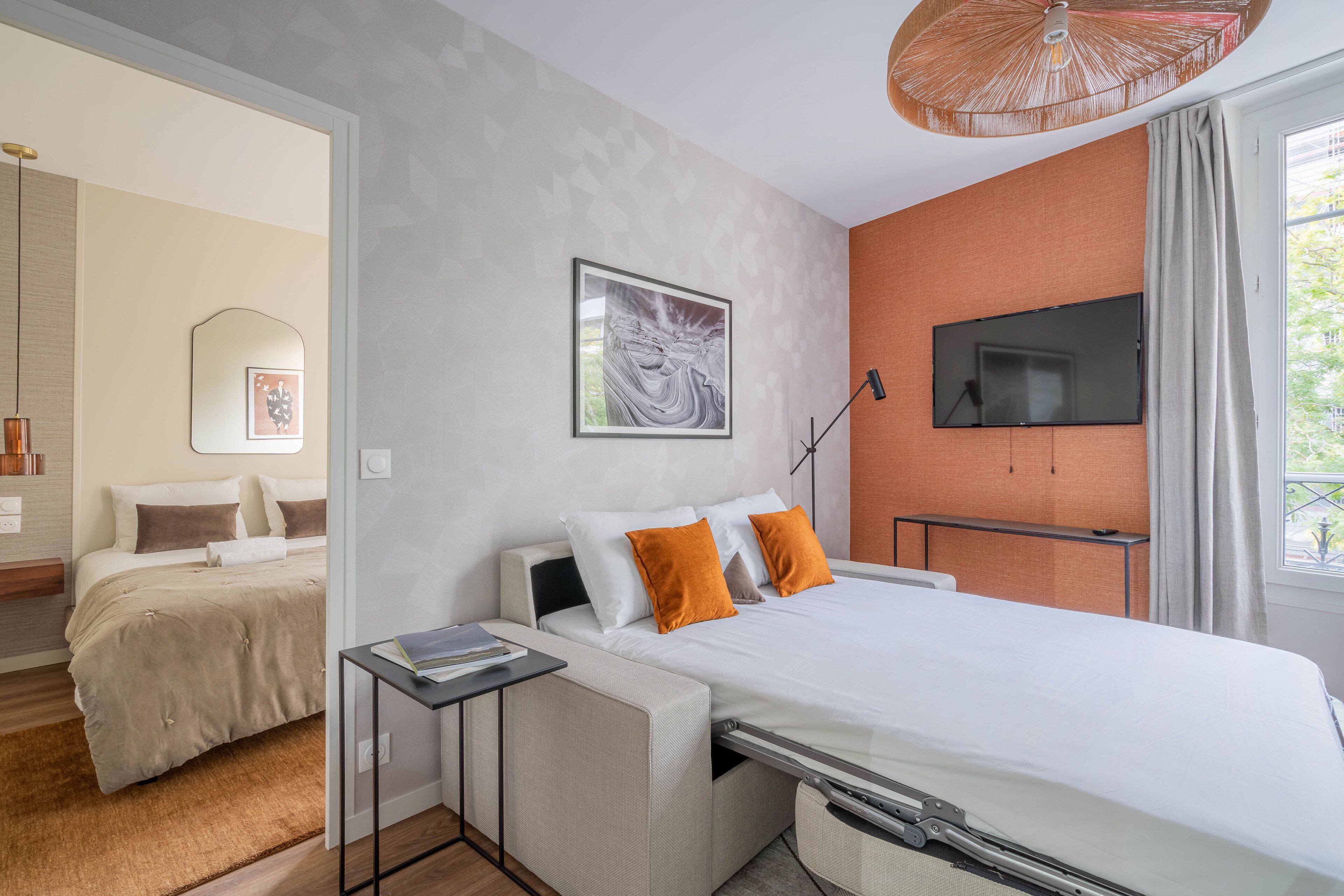 A modern hotel room with a bed, a desk, a TV, and a window with curtains.
