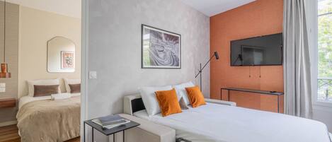 A modern hotel room with a bed, a desk, a TV, and a window with curtains.